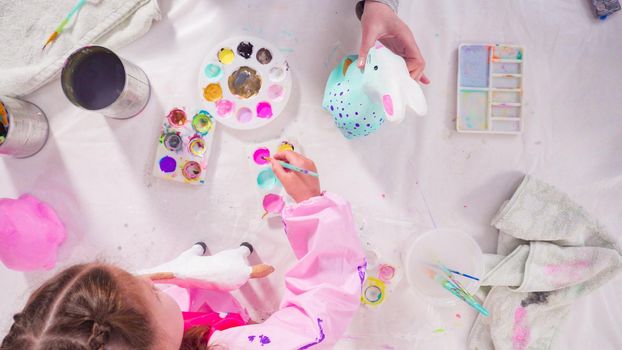 Flat lay. Little girl painting paper mache figurines with acrylic paint for her homeschooling art project.