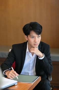 Thoughtful businessman sitting in his office room and looking out of window.