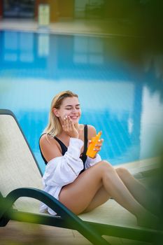 Attractive womav applying sunscreen on her face by the pool. Vacation sun protection factor