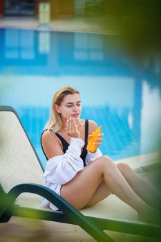 Attractive womav applying sunscreen on her face by the pool. Vacation sun protection factor