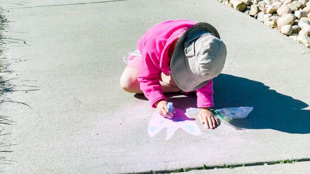 Little girl drawing with chalk on a sidewalk on the summer day.