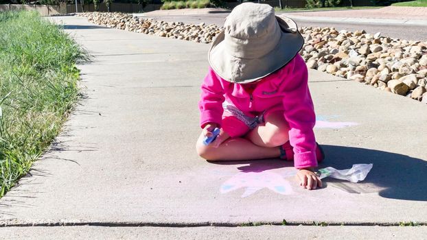Little girl drawing with chalk on a sidewalk on the summer day.