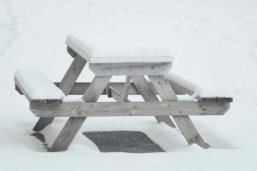 An empty bench in the park is covered with snow