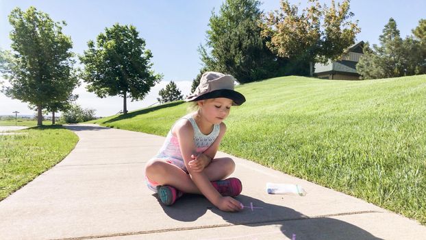 Little girl drawing with chalk on a sidewalk on the summer day.