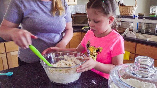 Little girl baking flatbread with her mother in the kitchen.