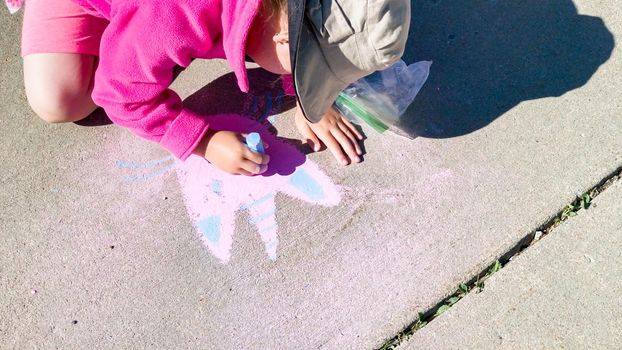 Little girl drawing with chalk on a sidewalk on the summer day.