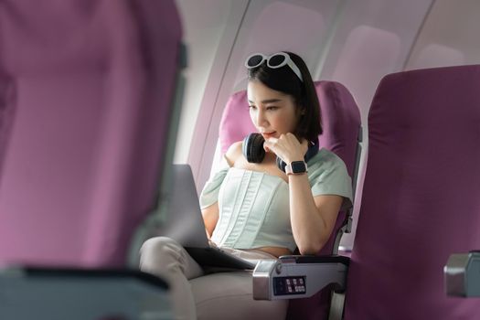 Joyful asian woman sits in the airplane and using laptop while go to travel.