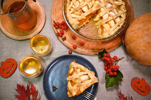 Still life: Healthy homemade baked pumpkin pie with caramelized apples and crispy crust, and cups of hot tea, surrounded by autumnal fallen leaves. Autumn time with healing drinks and sweet desserts