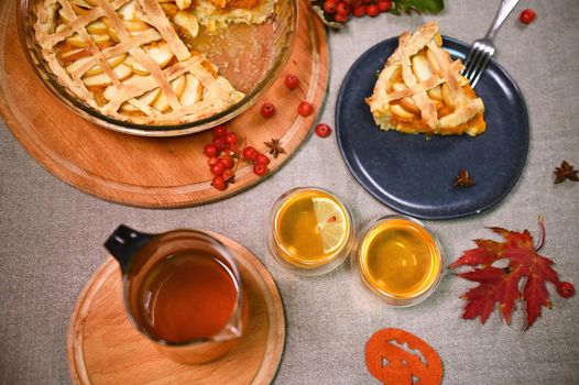 Still life. Homemade pumpkin pie with crispy crust and cups of healthy hot herbal tea, surrounded by viburnum berries, fallen maple leaves, pumpkin cut from felt paper on a linen tablecloth. Top view