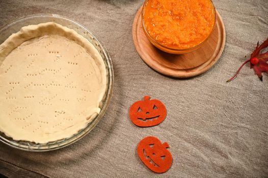 Still life. Top view of a rolled pastry dough in baking dish and fresh ingredients for making pumpkin apple Thanksgiving pie. Viburnum berries and red autumn maple leaf on table with linen tablecloth