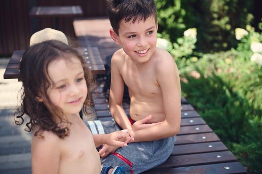 Charming adorable elementary age children, a boy and girl, brother and sister, friends talking together, playing on a summer terrace on a hot sunny summer day