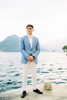 Groom in a suit stands on the pier against the backdrop of the mountains. High quality photo