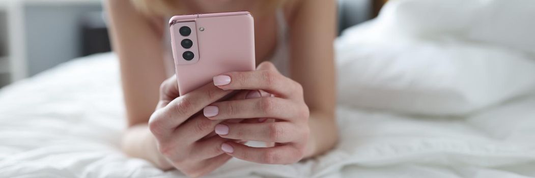 Young woman lying on bed and holding mobile phone in her hands closeup. Remote communication in social networks concept