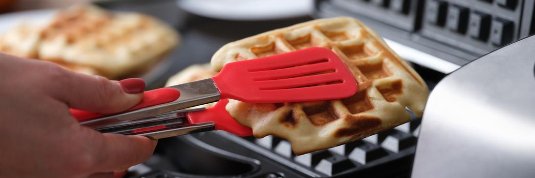 Cook taking out viennese waffle from multibaker using tongs closeup. Home baking concept