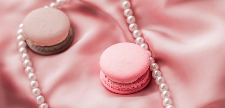 Girly, bakery and branding concept - Sweet macaroons and pearls jewellery on silk background, parisian chic jewelry, French dessert food and cake macaron for luxury confectionery brand, holiday gift