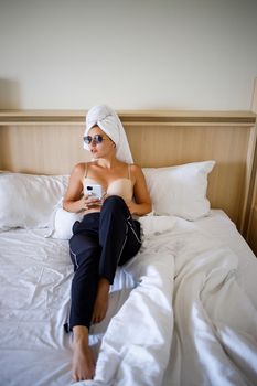 A beautiful young woman is lying in a large snow-white bed with a towel on her head.