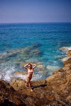 Young beautiful woman in a swimsuit stands on a rocky beach of the Mediterranean Sea. The concept of sea recreation. Selective focus