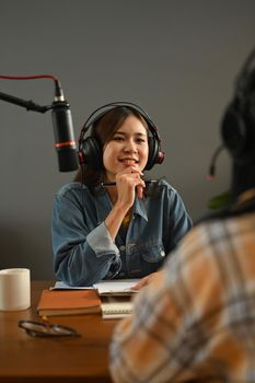 Friendly radio host in headphone discussing various topics with her guest while streaming live audio podcast from home studio.