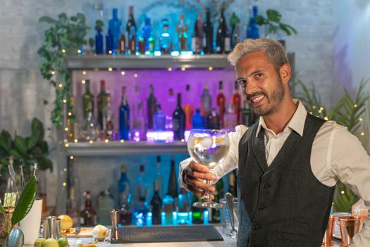 Elegant barman smiling on bar counter with a cocktail in his hand. Toasting in the air. High quality photo