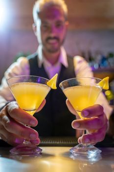 Barman serves two cocktails in the bar counter of the nightclub. High quality vertical photo