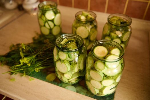 Top view of sterilized glass jars with pickled slices of ripe organic zucchini marinated in salt or vinegar brine, with fresh dill, garlic cloves. Food preservation. Canning. Preserving for the winter