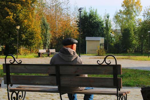 An elderly man sits on a bench in a city park.