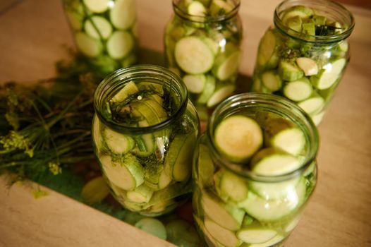 Top view of sterilized glass jars with pickled slices of ripe organic courgettes marinated in vinegar pickle, with fresh dill, garlic cloves. Food preservation. Canning. Preserving for the winter