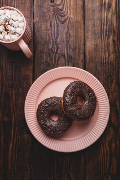 Two Chocolate Donuts and Mug of Hot Chocolate with Marshmallow on Rustic Wooden Surface. View from Above