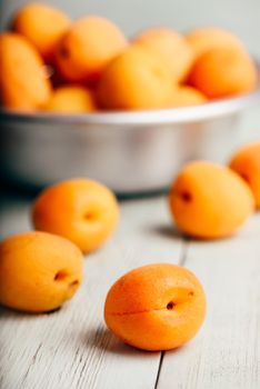 Mellow apricots over light wooden surface and metal bowl with fruits on background