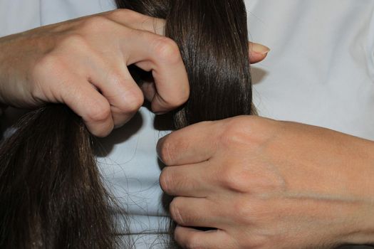 A girl with long dark hair is braiding her hair. Close-up hands. Hair care. Hair loss problem.