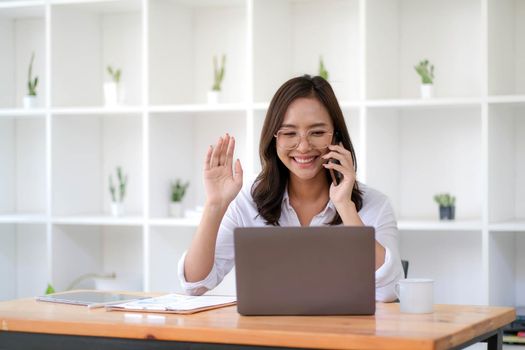 Beautiful Asian businesswoman having fun on the phone for a video call with a customer in the office..