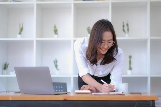 Asian Businesswoman Using laptop computer and working at office with calculator document on desk, doing planning analyzing the financial report, business plan investment, finance analysis concept..