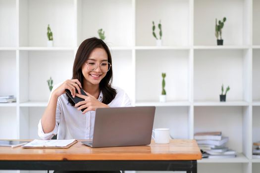 Charming young Asian businesswoman sitting at work holding pen using graph document at office.