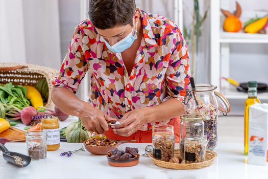 Woman wearing a medical mask, preparing dried fruits, cereals, and seeds vegetable milk, tea, honey, citrus etc.