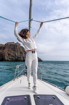 Woman standing on the nose of the yacht at a sunny summer day, breeze developing hair, beautiful sea on background.