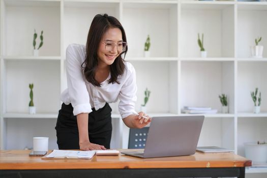 Portrait of smiling beautiful Asian businesswoman enjoy the idea sitting with laptop computer at office..