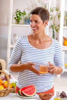 Woman, a cup of tea in hand, surrounded by cereals, fresh fruit and dried fruit, honey,