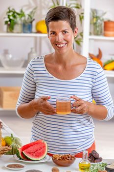 Woman, a cup of tea in hand, surrounded by cereals, fresh fruit and dried fruit, honey,