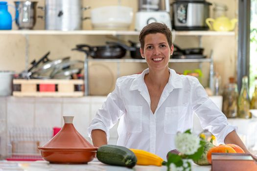 Relaxed woman, with a bunch of organic vegetables in front and back the kitchen utensils in blur.