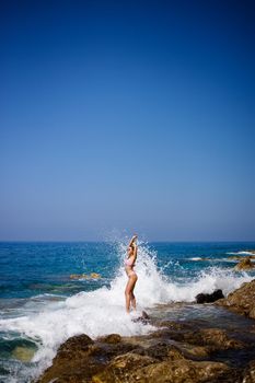 Beautiful young woman in a swimsuit on a rocky beach on a sunny day against the backdrop of waves. Vacation in the summer season. Selective focus