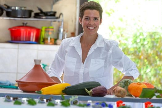 Young woman smiling behind a worktop supporting vegetables from the vegetable garden for tagine.