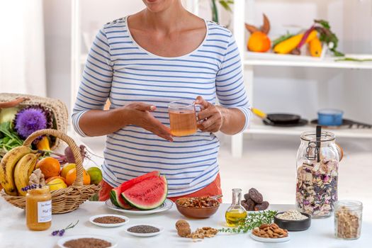 Woman, face cut a cup of tea in hand, surrounded by cereals, fresh fruit and dried fruit, honey,