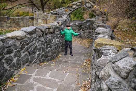 Portrait of boy kid a walk under a brick bridge and looking up, child walking outside, Young boy relaxing outdoors in autumn on bridge. Tourism concept.