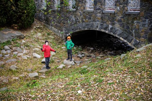 Portrait of two boys kid a walk under a brick bridge and looking up, child walking outside, Young boys relaxing outdoors in autumn on bridge. Tourism concept.