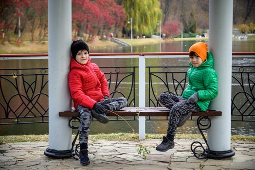 Two siblings stand on the bridge and admire the magnificent view of the autumn forest and its reflection in the lake water. Autumn walk. Outdoor lifestyle, active family lifestyle.