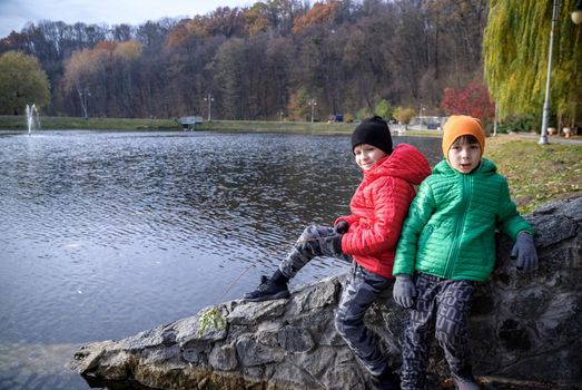 Two siblings stand on the bridge and admire the magnificent view of the autumn forest and its reflection in the lake water. Autumn walk. Outdoor lifestyle, active family lifestyle.