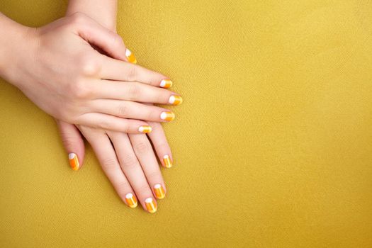 Beautiful Female Hands with bright Orange Manicure like Candy Corn on Yellow Background. Manicured Nails with Creative Gel Polish Design. Halloween Style