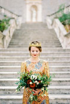 Bride in a golden dress and crown stands on the steps with a bouquet. High quality photo