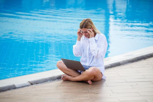 Young woman businessman with laptop sitting by the pool. Open workplace. Freelancer concept. Online shopping. Vacation work