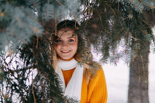 Teen blonde in a yellow sweater outside in winter. A teenage girl on a walk in winter clothes in a snowy forest.